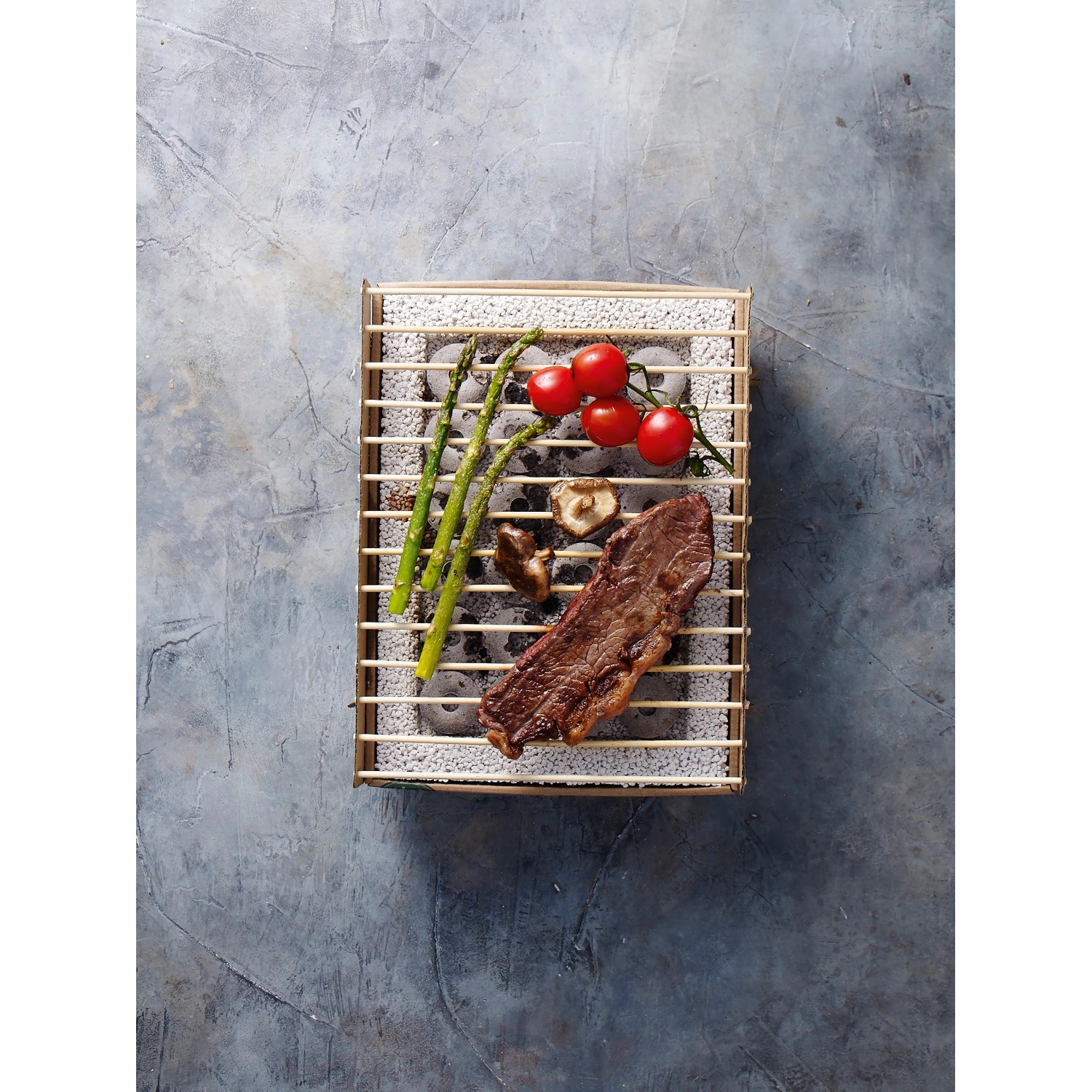 Einweg Casus Grill mit Steak, Tomaten und Gemüse auf dem Grillrost.