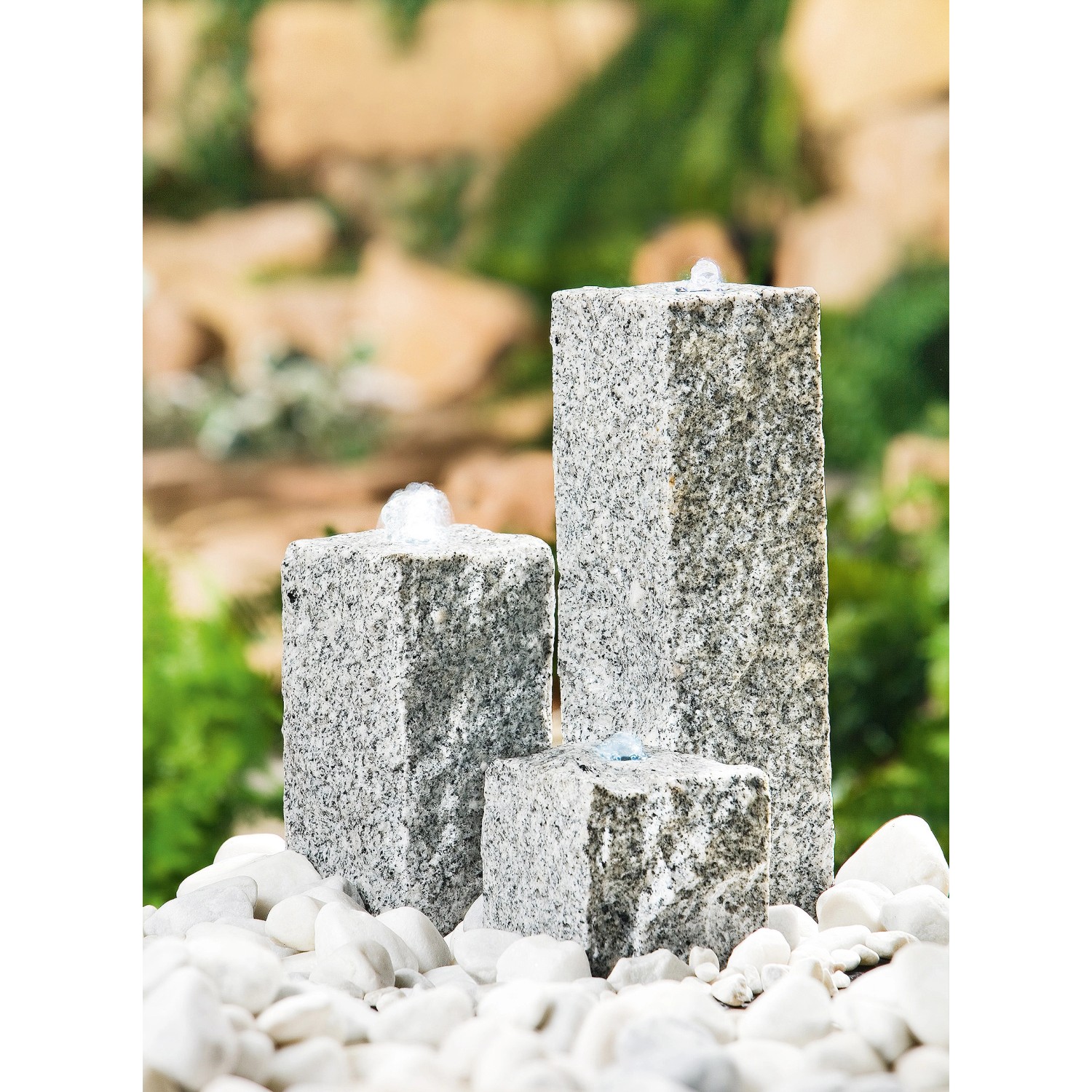 Heissner Wasserspiel mit drei grauen Granit-Säulen und weißen Kieselsteinen im Garten.