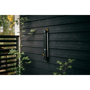 Fiskars Oszillierender Regner Comfort S-L, schwarz-orange, zur Gartenbewässerung an dunkler Holzwand.