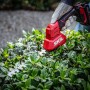 Skil Akku-Gras- und Strauchschneider 0631CA in Nutzung, rot/schwarz, schneidet Hecke.