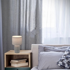 Graue Brilo Tischleuchte Ino mit Keramikfuß und Stoffschirm auf Nachttisch.