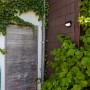 Mattschwarze Lutec LED Solar Wandleuchte Try an Hauswand mit Pflanzen.