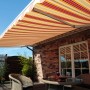 Gelenkarmmarkise Star Fix, 300x250 cm, orange-rot gestreift, montiert auf einer Terrasse.