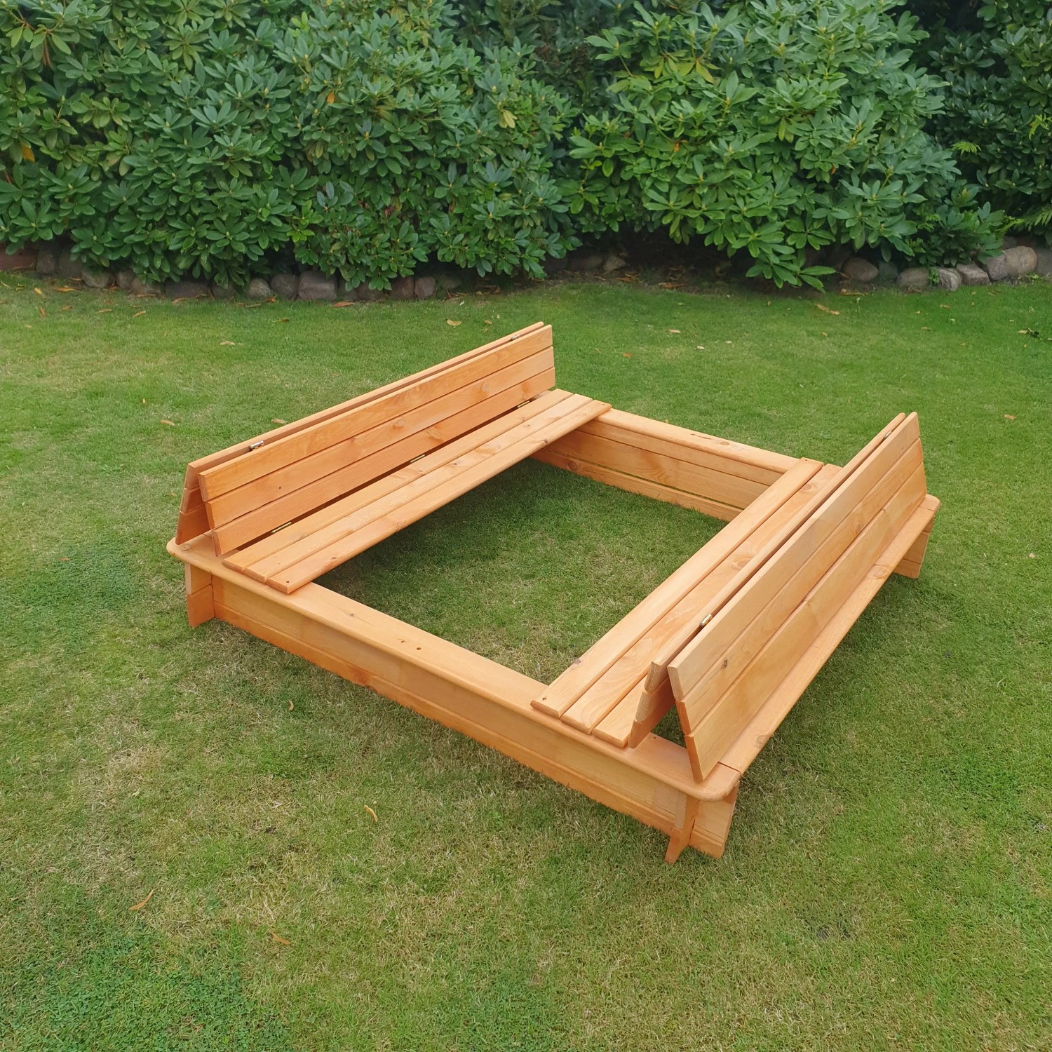 Holz Sandkasten Donald 140x140 cm mit klappbarer Abdeckung als Sitzbank im Garten.