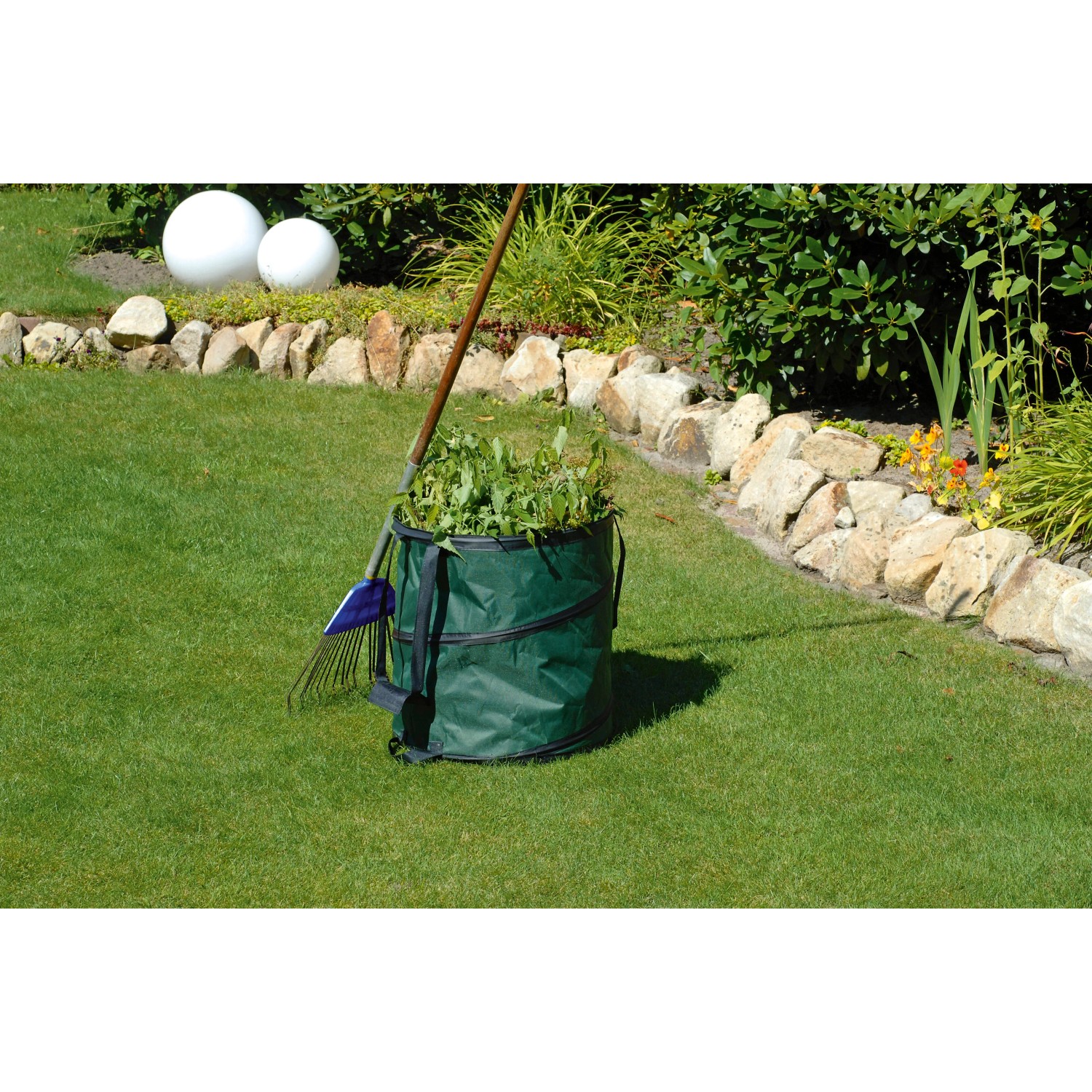 Grüner Gartensack Pop Up (85 l) mit Gartenabfällen und Rechen auf Rasen.