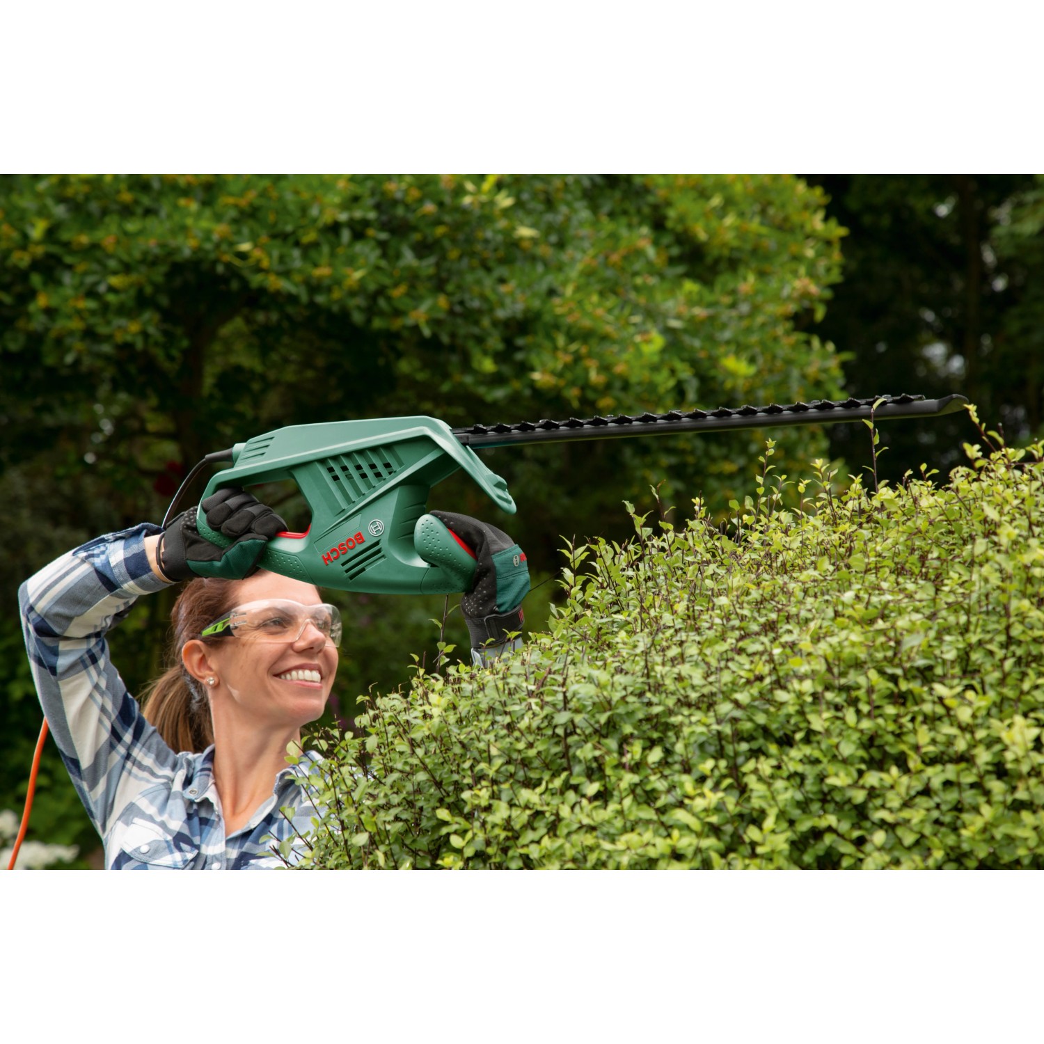 Frau schneidet Hecke mit Bosch Elektro-Heckenschere EasyHedgeCut 45. Das Gerät ist grün und schwarz.