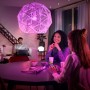 Philips Hue E27 Lampe, farbiges Licht im Wohnraum mit Personen am Tisch.