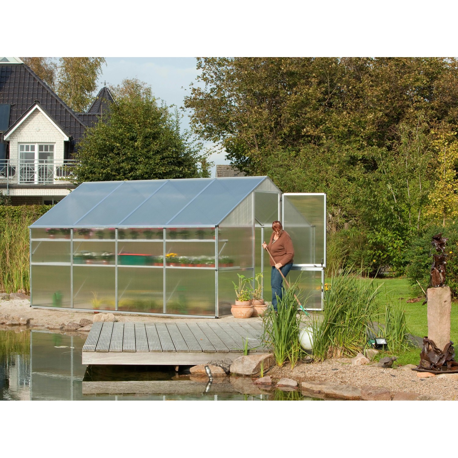 KGT Gewächshaus Orchidee Alu blank 12,74 m² mit geöffneter Tür und Frau im Garten.