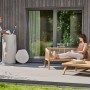Garantia Regentonne Woodstock Baumstamm 250 l Greywood im Garten mit Person beim Wasser holen.