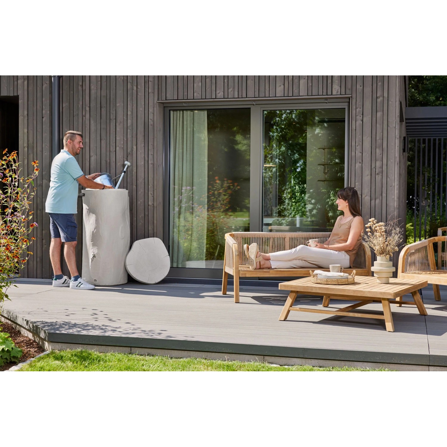 Garantia Regentonne Woodstock Baumstamm 250 l Greywood im Garten mit Person beim Wasser holen.