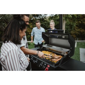 Enders Plancha Gussplatte XL auf Grill mit Speisen und Personen im Hintergrund.
