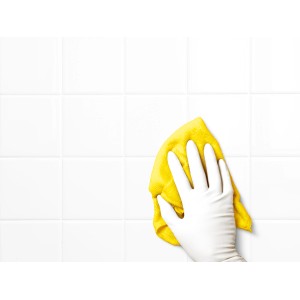 Hand mit weißem Latex-Einweghandschuh reinigt weiße Fliesen mit gelbem Tuch.