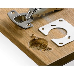 Hettich Reparaturblech (weiß) für 35 mm Topfscharnier auf Holzplatte mit beschädigtem Bohrloch.