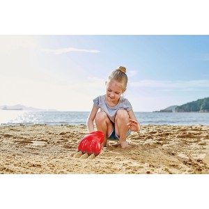 Kind spielt mit roter Hape Power-Klaue im Sand am Strand. Sandspielzeug für Spiel & Spaß.