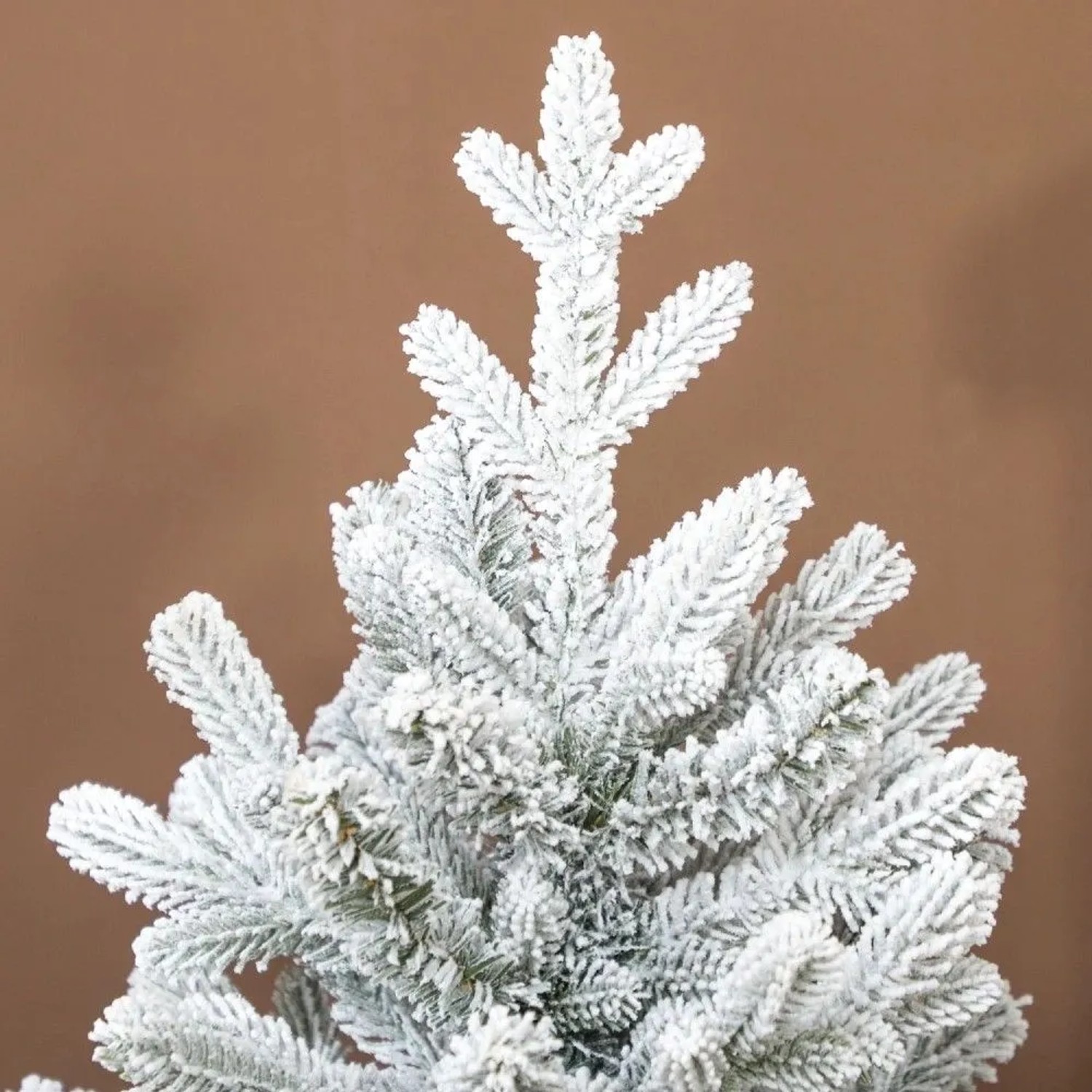 Nahaufnahme eines künstlichen Weihnachtsbaums mit dicht verschneiten grünen Zweigen. Perfekt für festliche Weihnachtsdekoration.