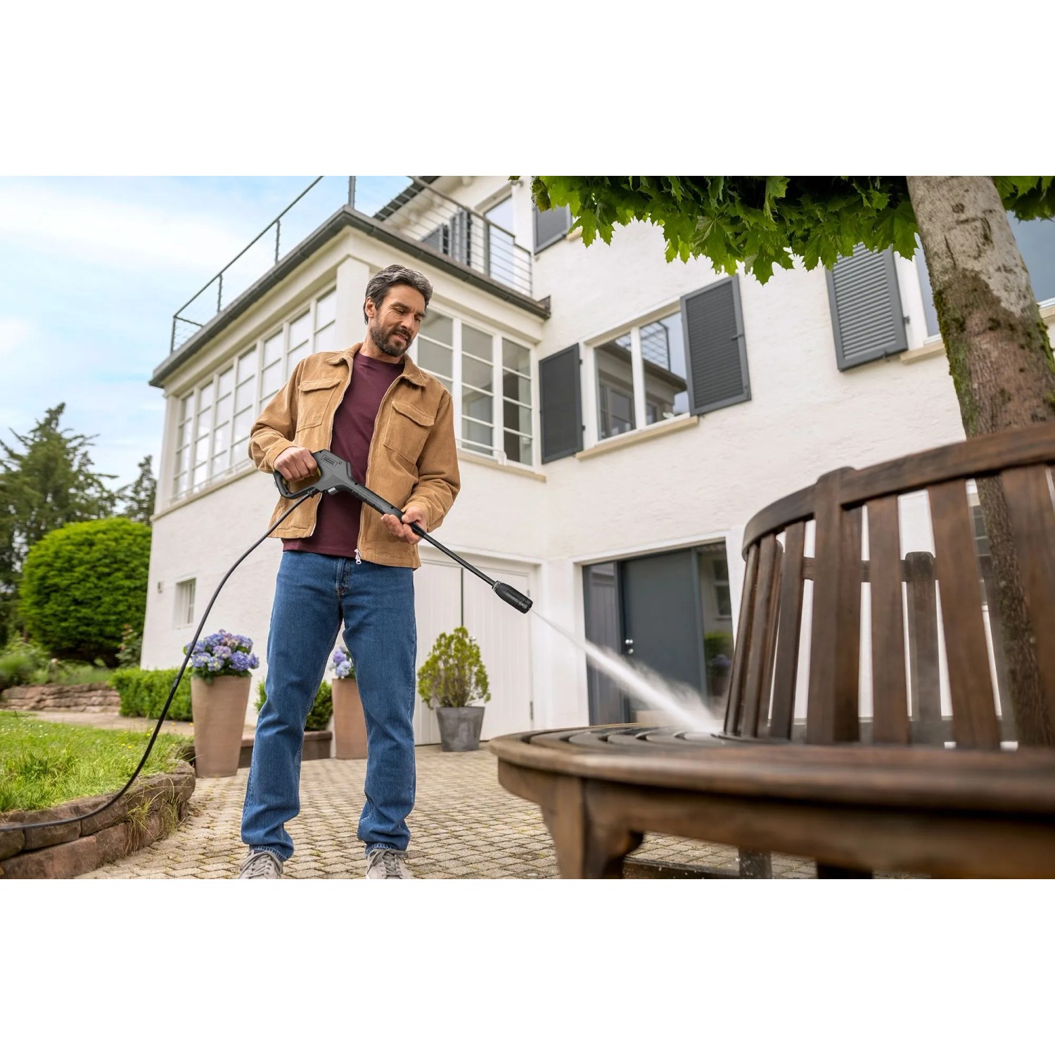 Mann reinigt Holzbank mit Kärcher Hochdruckreiniger K 3 Premium auf Terrasse. Ideal für Haus- & Gartenreinigung.