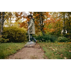 Frau benutzt Fiskars Ergonomic Fächerbesen zum Laubsammeln im Garten.