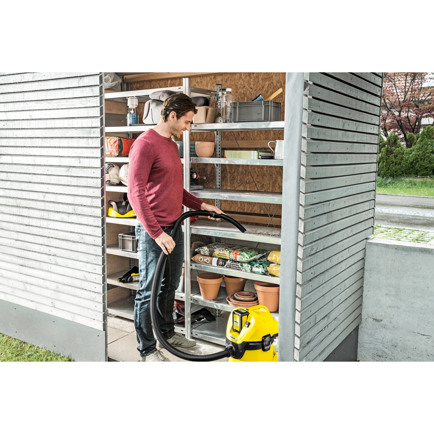 Mann saugt mit gelbem Kärcher Akku-Mehrzwecksauger WD 3 Battery ein Regal im Gartenhaus.