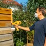 Mann sprüht mit Wagner Farbsprühsystem W 125 Holzschutz auf einen Zaun.