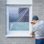 Mann befestigt LUX Fensterschutzfolie am Fensterrahmen. Schutzfolie für Renovierungsarbeiten.