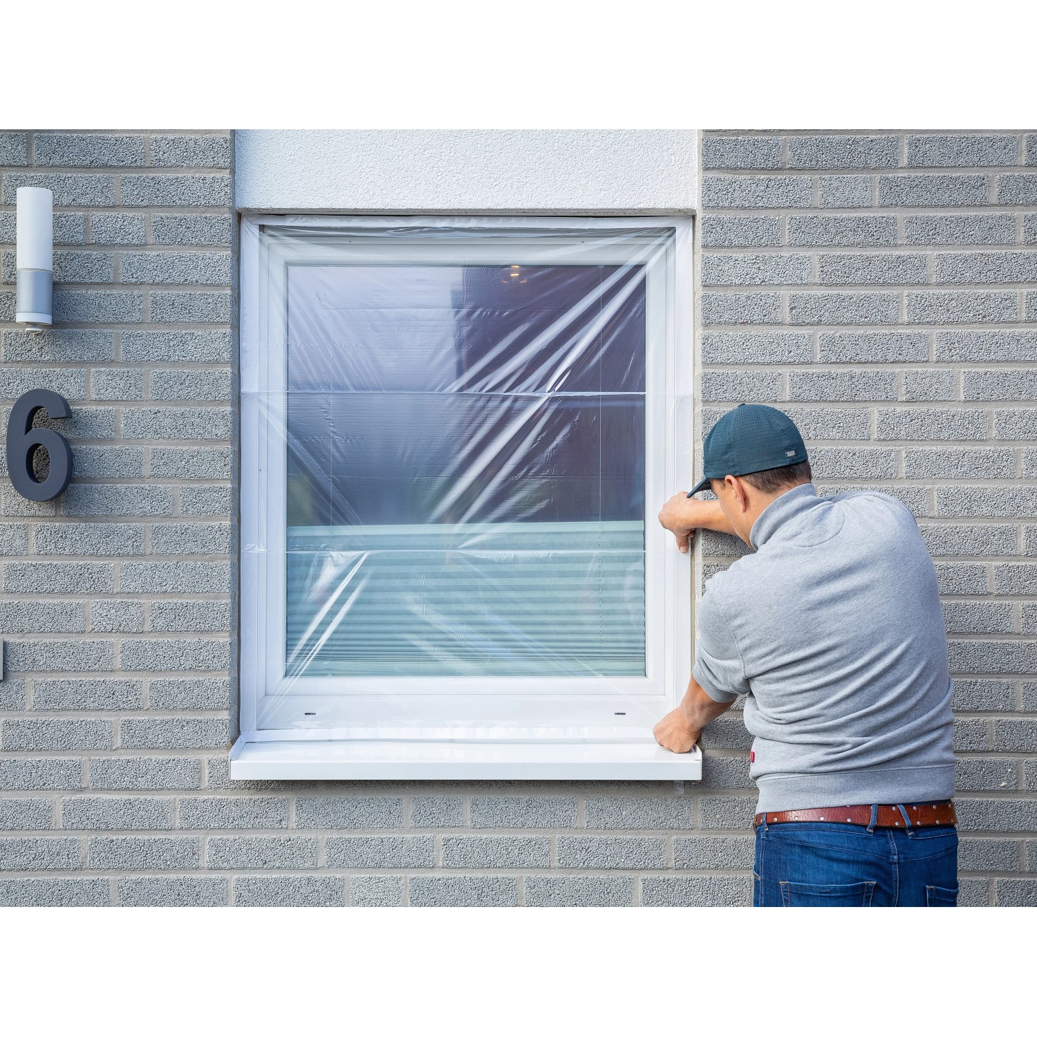 Mann befestigt LUX Fensterschutzfolie am Fensterrahmen. Schutzfolie für Renovierungsarbeiten.