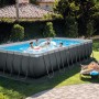Rechteckiger Intex Frame Pool Ultra Quadra XTR mit Stahlrahmen, Badegästen und Liegen im Garten.