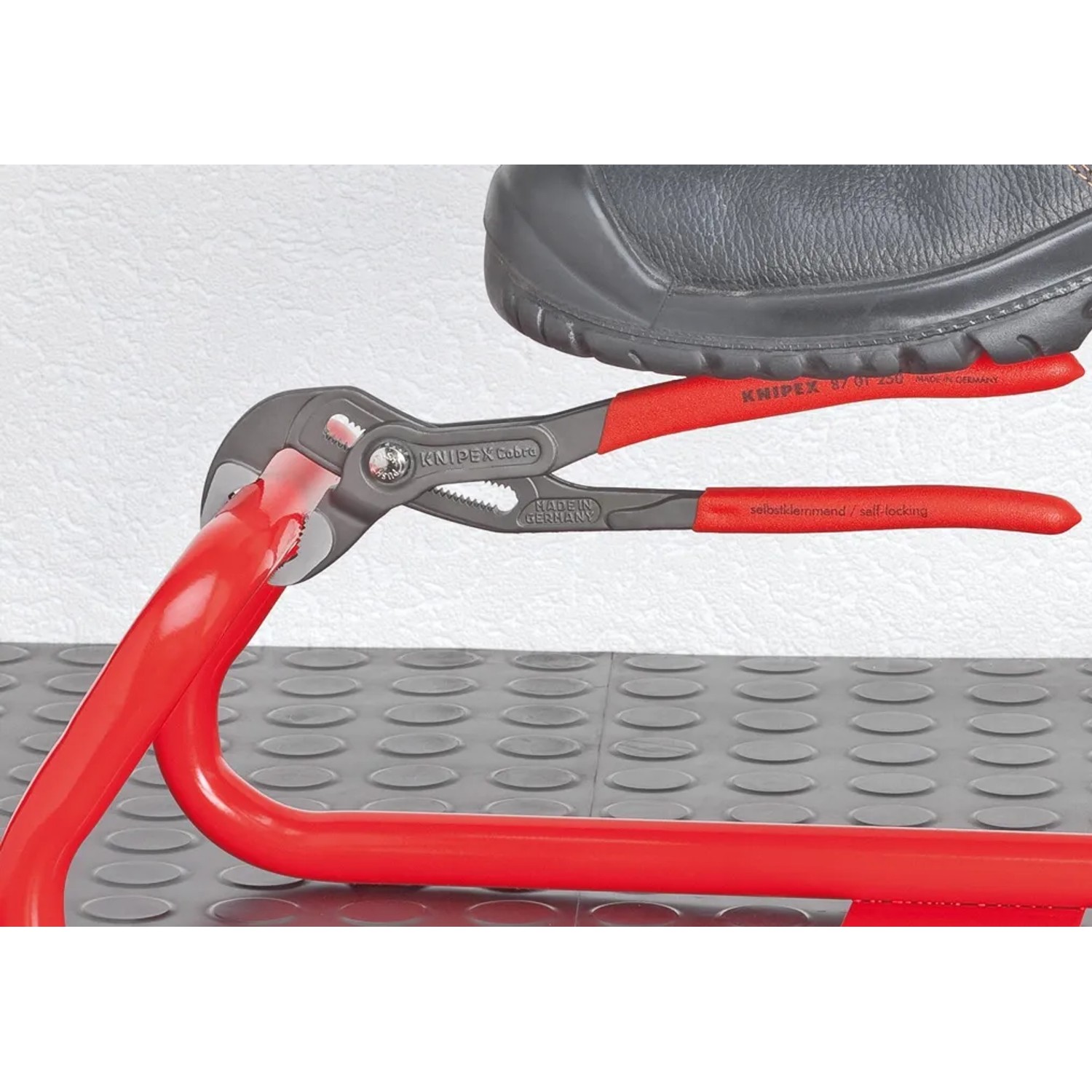 Knipex Cobra Rohrzange 300 mm beim Greifen eines roten Rohrs, mit Fuß auf dem Griff für zusätzlichen Druck.