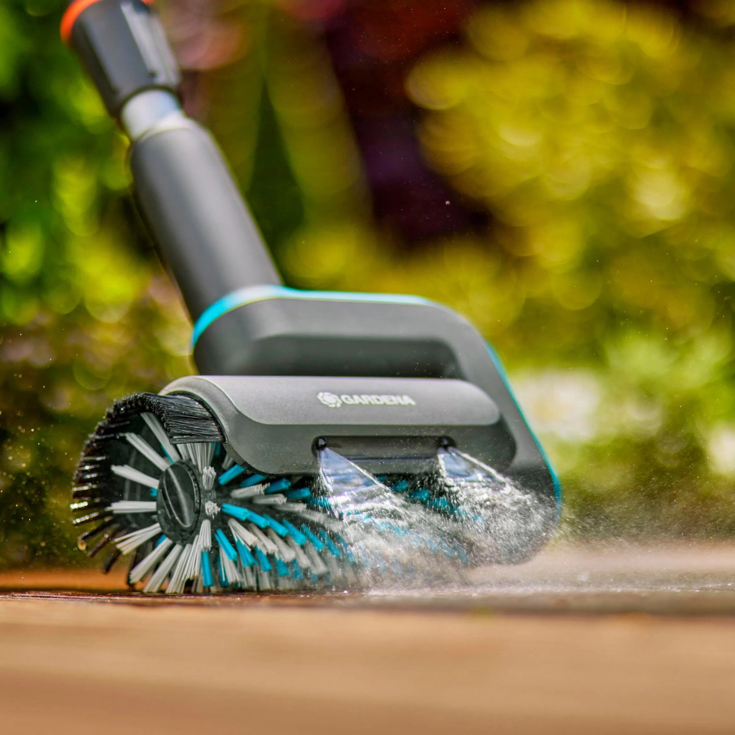 Gardena AquaBrush Universal Akku-Multi-Reiniger in Aktion mit Wasserstrahl auf Holzterrasse.
