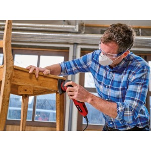 Mann mit Schutzbrille schleift mit rotem Einhell Deltaschleifer eine Holzstuhl-Lehne. Ideal für Möbel und schwer zugängliche Stellen.