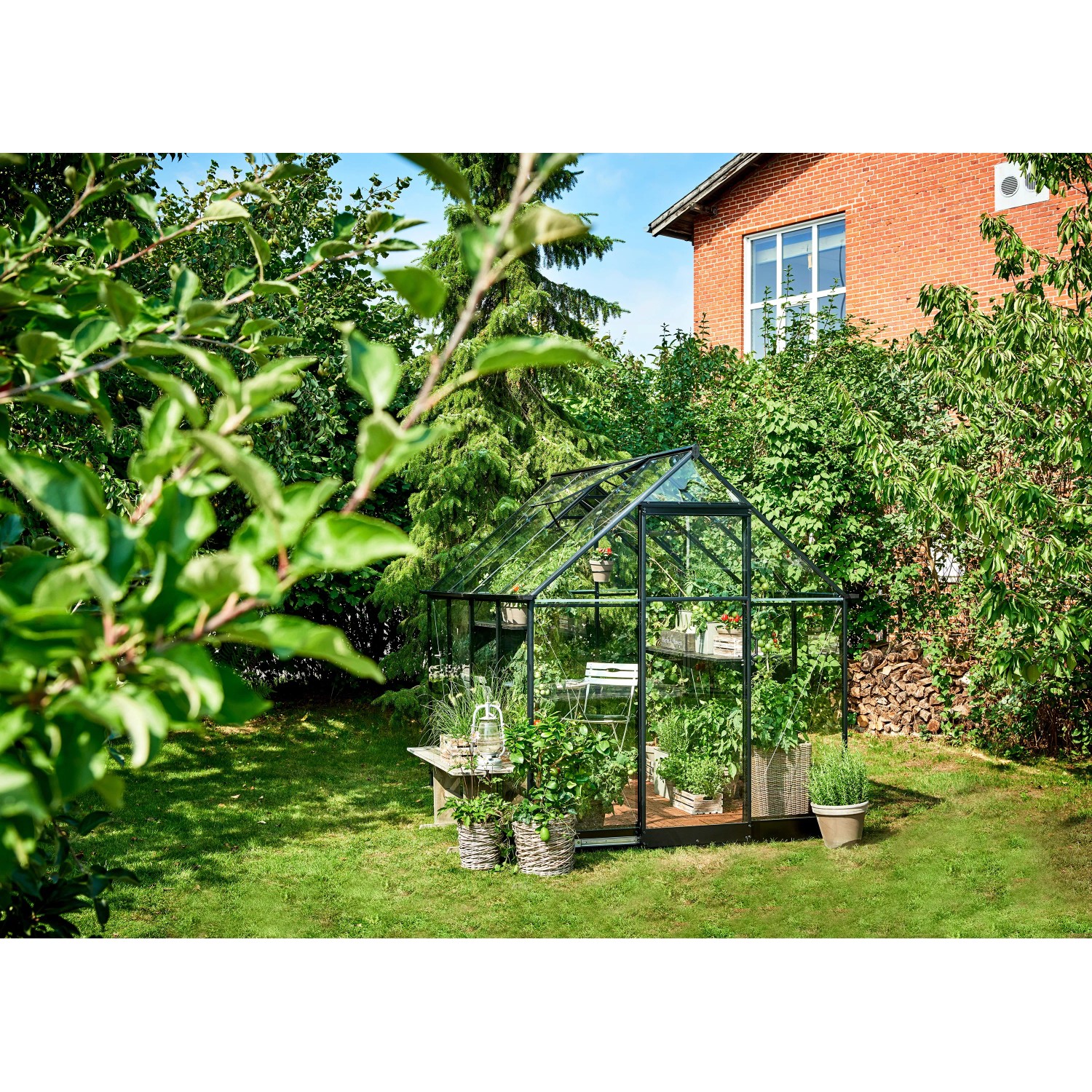 Schwarzes Halls Gewächshaus Qube 68 (5 m²) im Garten mit Pflanzen.
