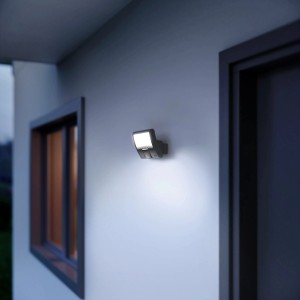 Angeschalteter Steinel LED-Außenwandstrahler XLED Curved S mit Bewegungsmelder an Hauswand.