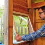 Mann montiert transparente Verglasungsfolie (125 cm) an einem Holzrahmen. Kunststoffbedachung für klare Sicht.