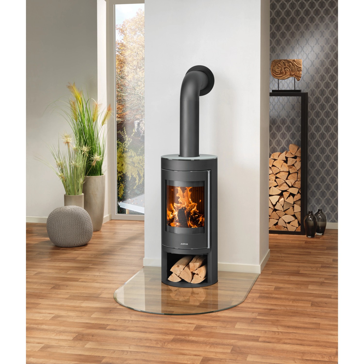 Schwarzer Justus Kaminofen Mino 2.0 mit Glasabdeckung und Holzscheiten im Wohnraum.