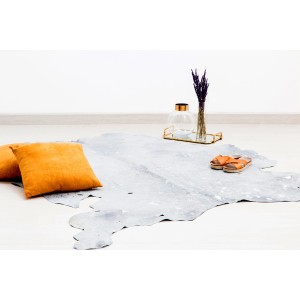 Grau-silberner Kayoom Teppich Fly 120x190 cm aus Leder, mit Kissen und Deko auf hellem Boden.