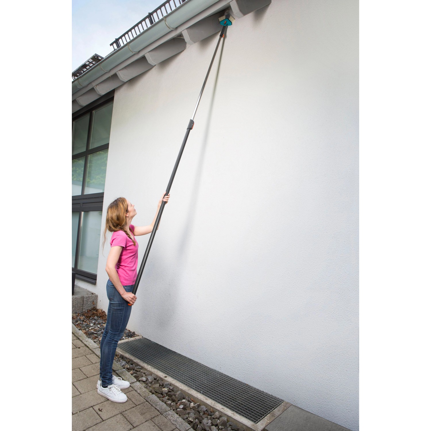 Frau nutzt Gardena combisystem Winkelbesen mit Stiel zur Reinigung einer Dachrinne.