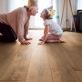 Verlegter Laminatboden Kronoflooring Gold Volcano Oak mit spielender Familie im Wohnraum.