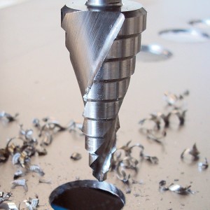 HSS-Stufenbohrer (4-20 mm) mit Sechskantschaft bohrt Loch in Metall, Späne liegen herum.