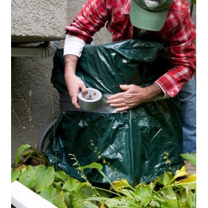 Mann fixiert grüne Plane mit Duck Tape Gewebe-Klebeband Silber an einer Außeneinheit.