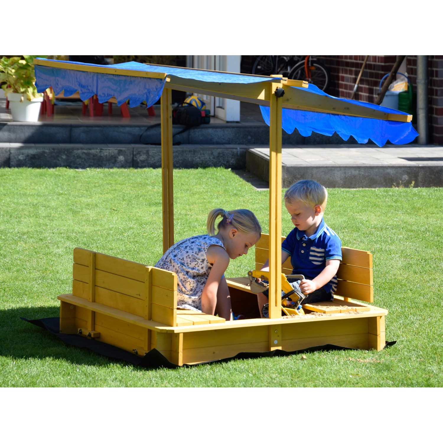 Dobar Sandkasten mit Dach, gelbes Holz, blaue Markise, zwei Kinder spielen im Garten.