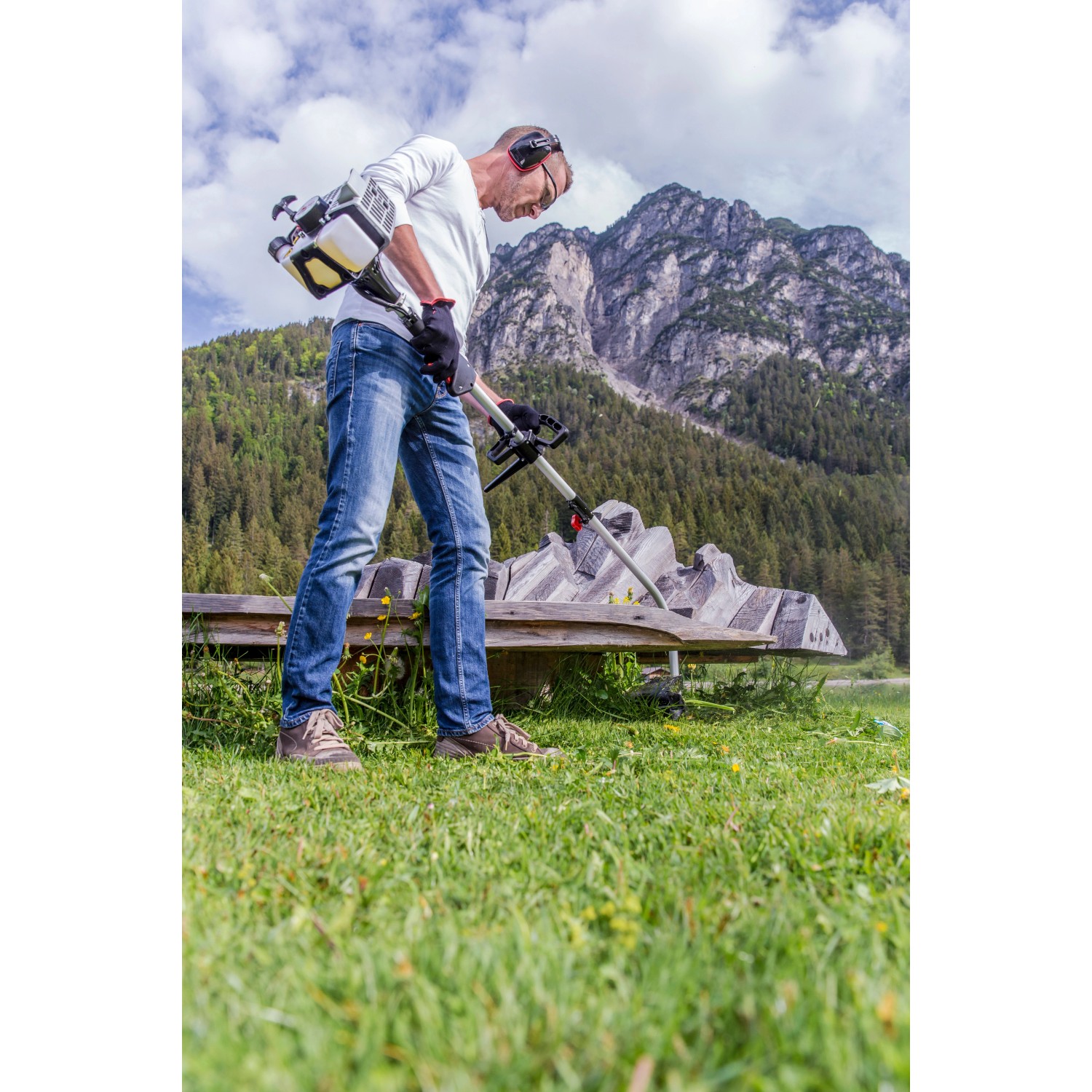 Mann arbeitet mit Al-Ko Benzinmotorsense BC 223 L-S im Garten vor Bergkulisse.