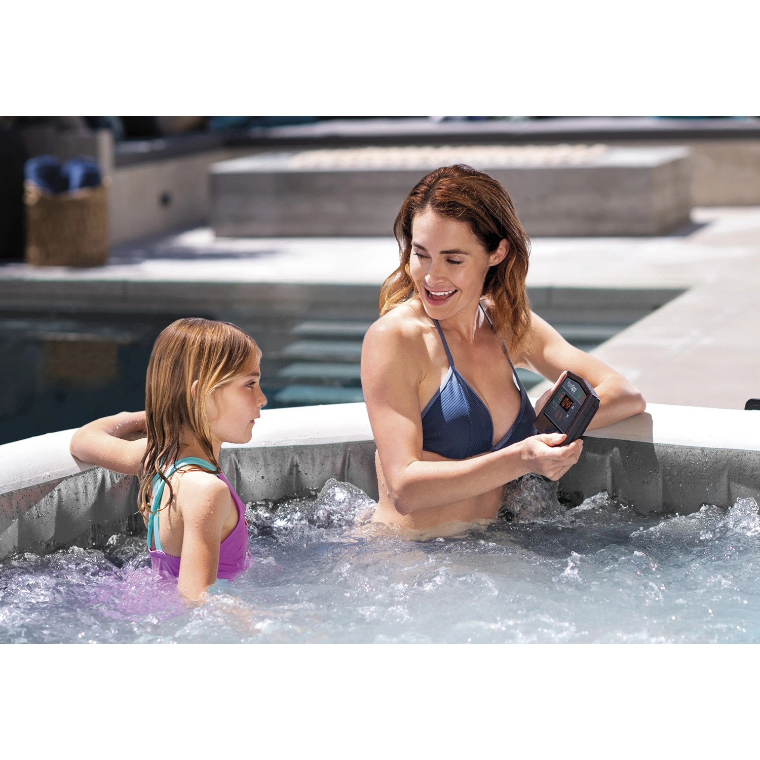 Intex Greywood Deluxe aufblasbarer Whirlpool mit zwei Personen im Wasser, davon eine mit Steuereinheit.