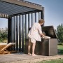 Dunkelgraue Biohort Loungebox 160 auf Holzterrasse, Mann verstaut Kissen. Regenwasserdichte Universalbox für Gartenzubehör.