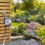 Gardena Bewässerungscomputer Master am Wasserhahn mit Garten im Hintergrund.
