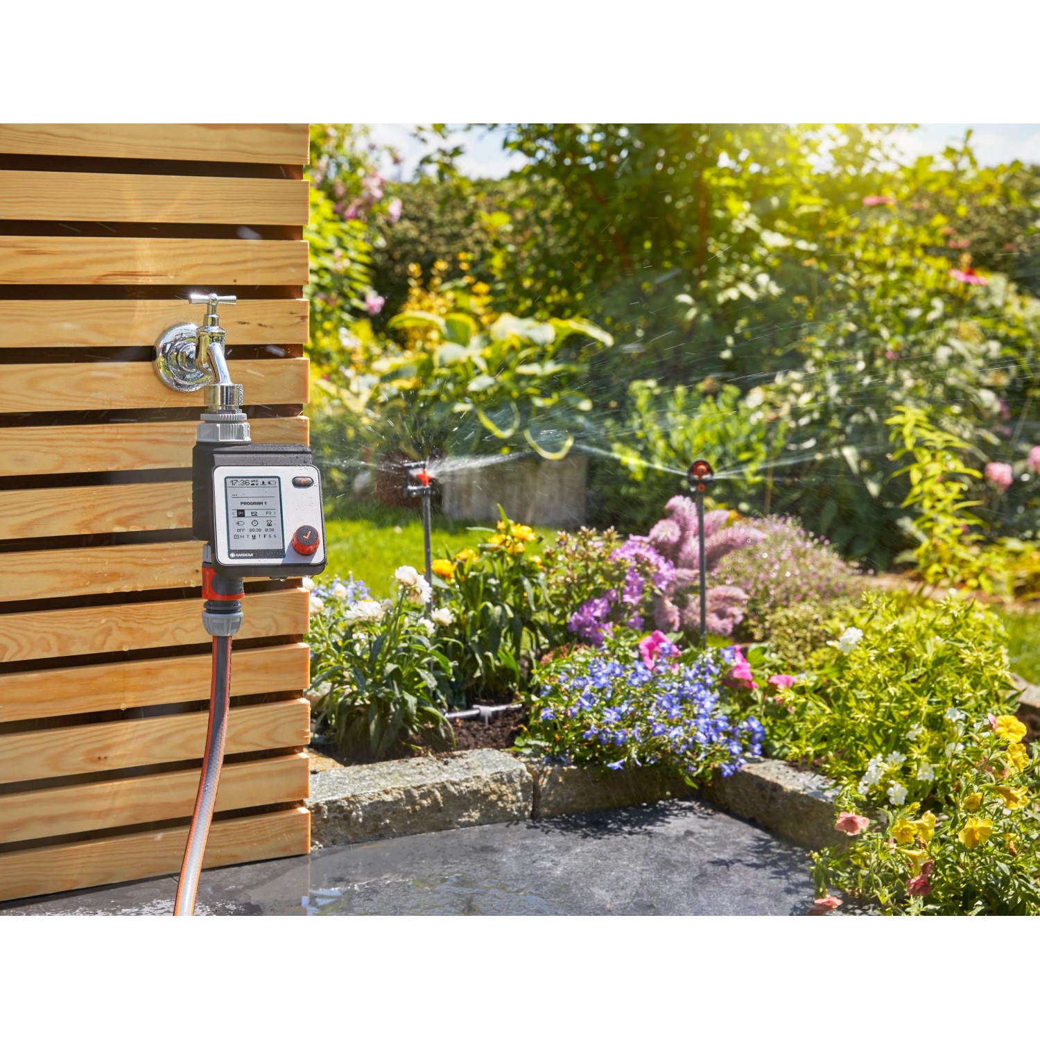 Gardena Bewässerungscomputer Master am Wasserhahn mit Garten im Hintergrund.