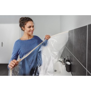 Frau befestigt Tesa Abdeckfolie mit Klebeband im Bad. Schutz vor Farbe bei Renovierung.