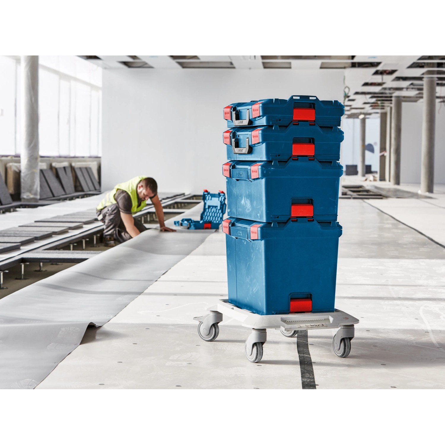 Gestapelte blaue Bosch Professional L-Boxx Werkzeugkoffer auf Rollbrett im Rohbau.