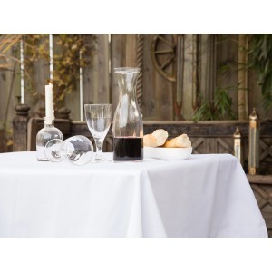 Weiße Floracord Tischdecke 110x140 cm auf gedecktem Tisch mit Gläsern, Karaffe und Brot.