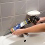 Hände verfugen ein weißes Waschbecken mit Soudal Sanitär Silikon transparent aus einer Kartuschenpistole im Bad.