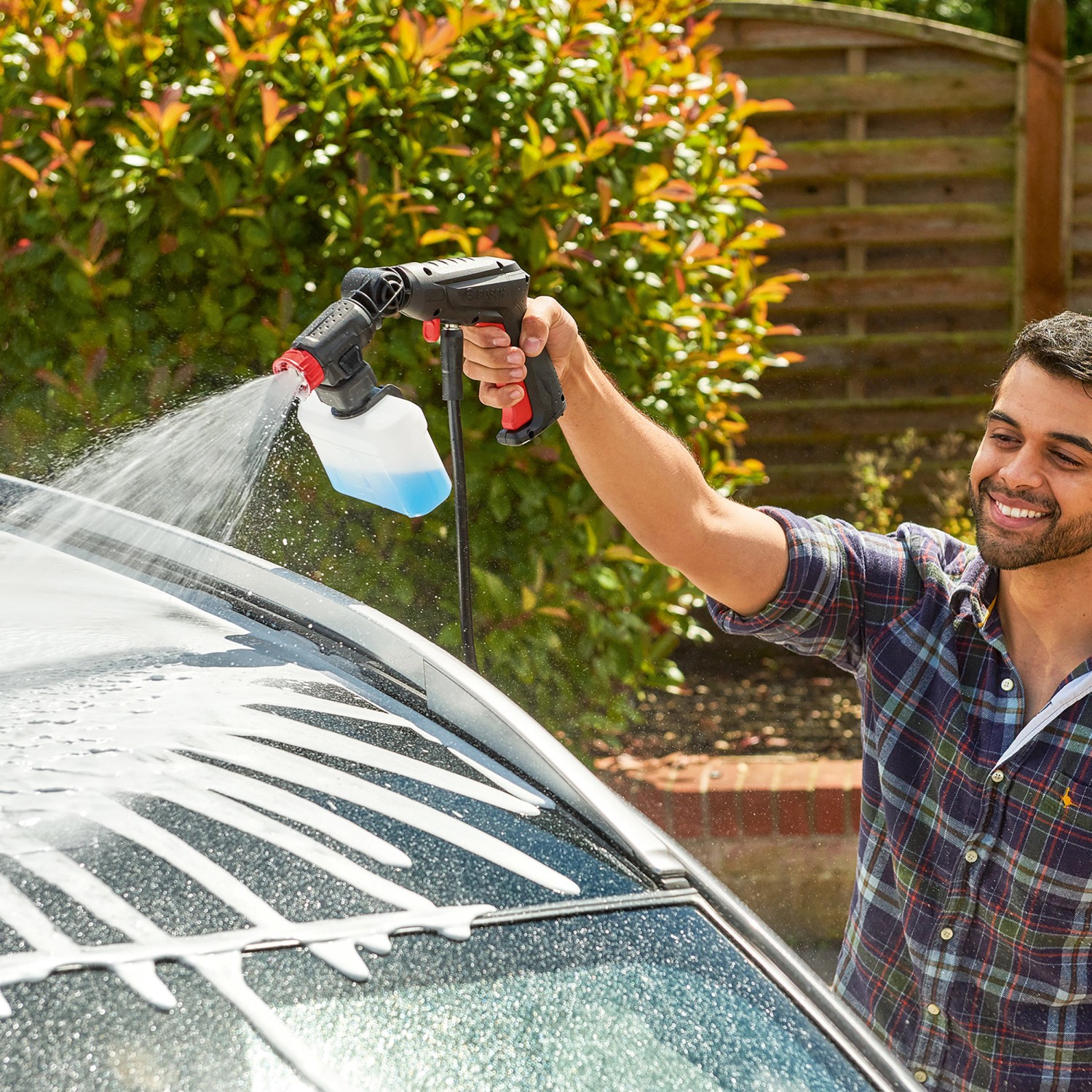 Mann reinigt Auto mit Bosch EasyAquatak 100 Hochdruckreiniger mit Reinigungsmitteldüse.