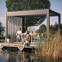 Biohort Pergola in Dunkelgrau/Silber-Metallic auf Holzsteg am See mit sitzenden Personen.